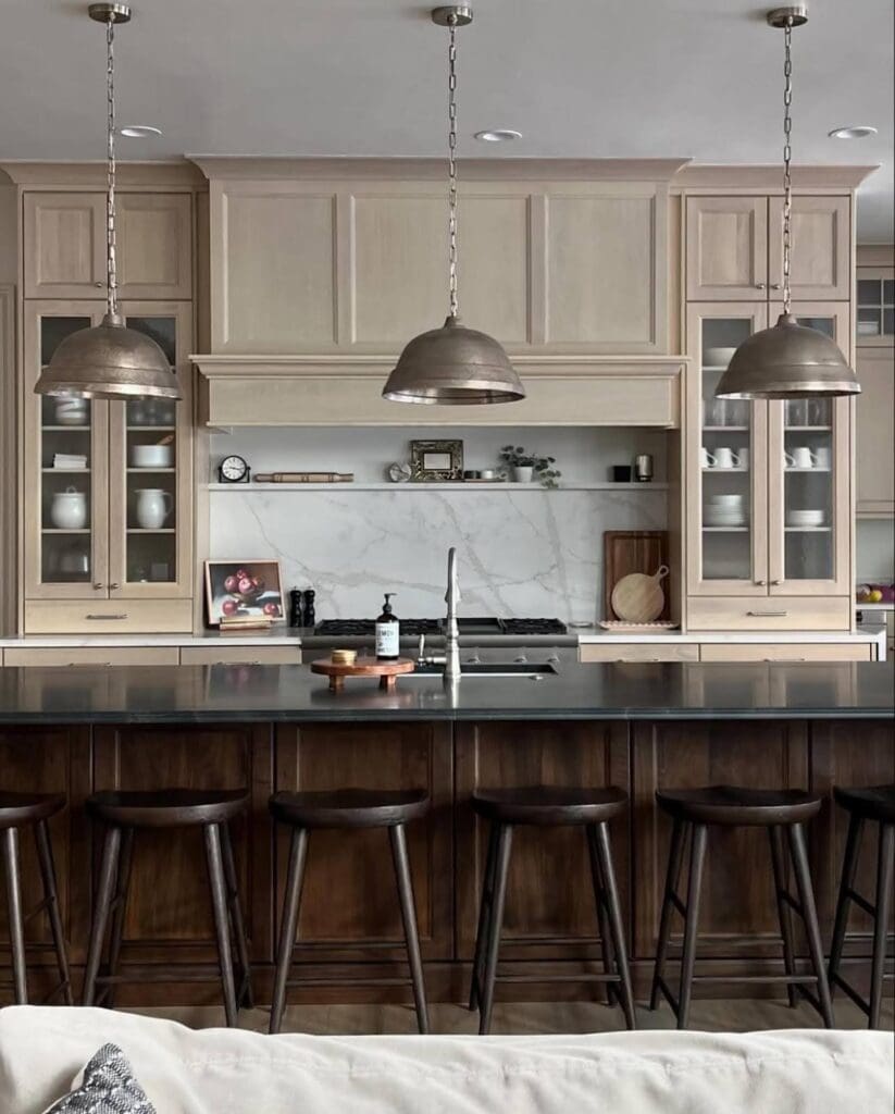 Kitchen island in rich dark wood with black countertop, paired with light wood cabinetry and metal pendant lights