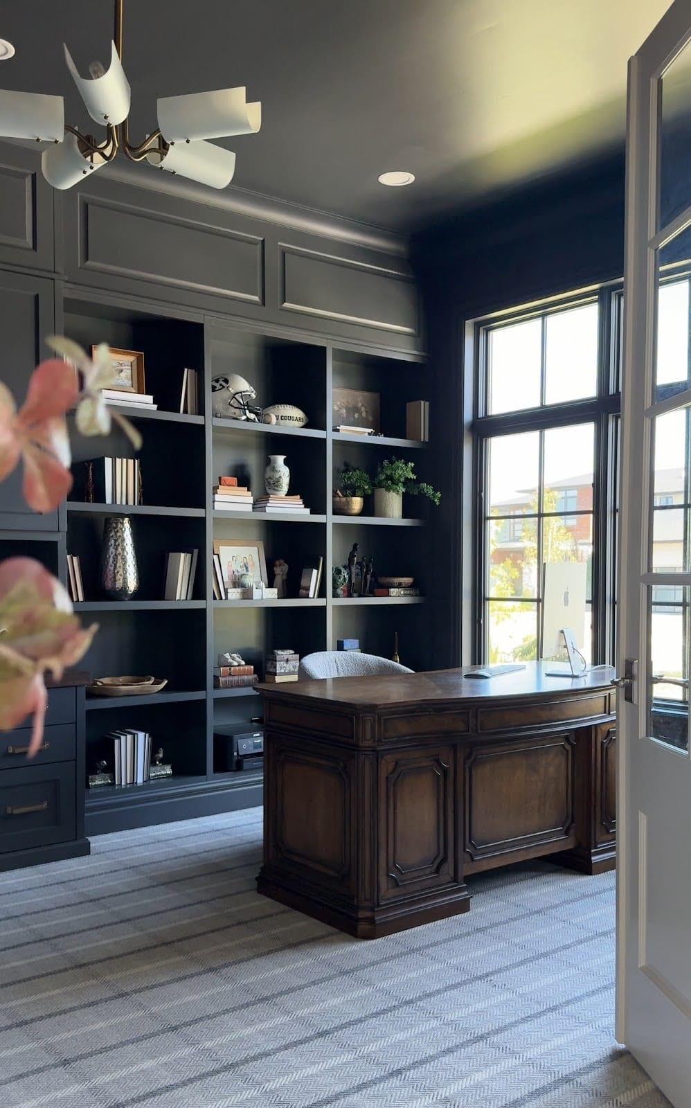 Home office with dark built-in shelves and rich wood executive desk for a warm, moody workspace.