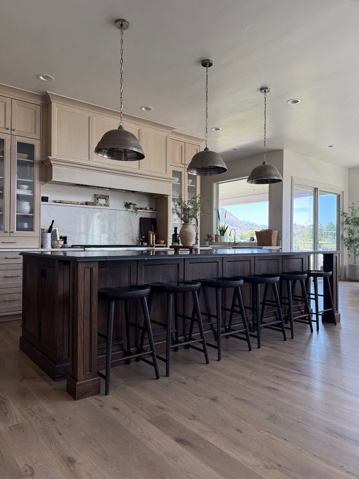 Large kitchen with dark-stained island base, black counter stools, and natural wood cabinetry.
