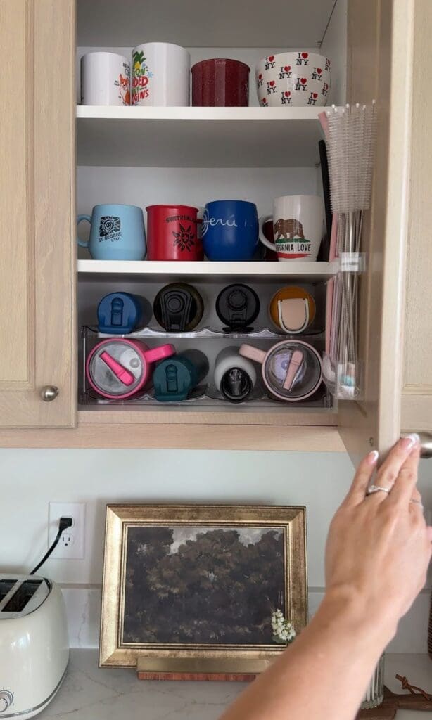 Close-up of organized cabinet with mugs, tumblers, and the mounted straw organizer
