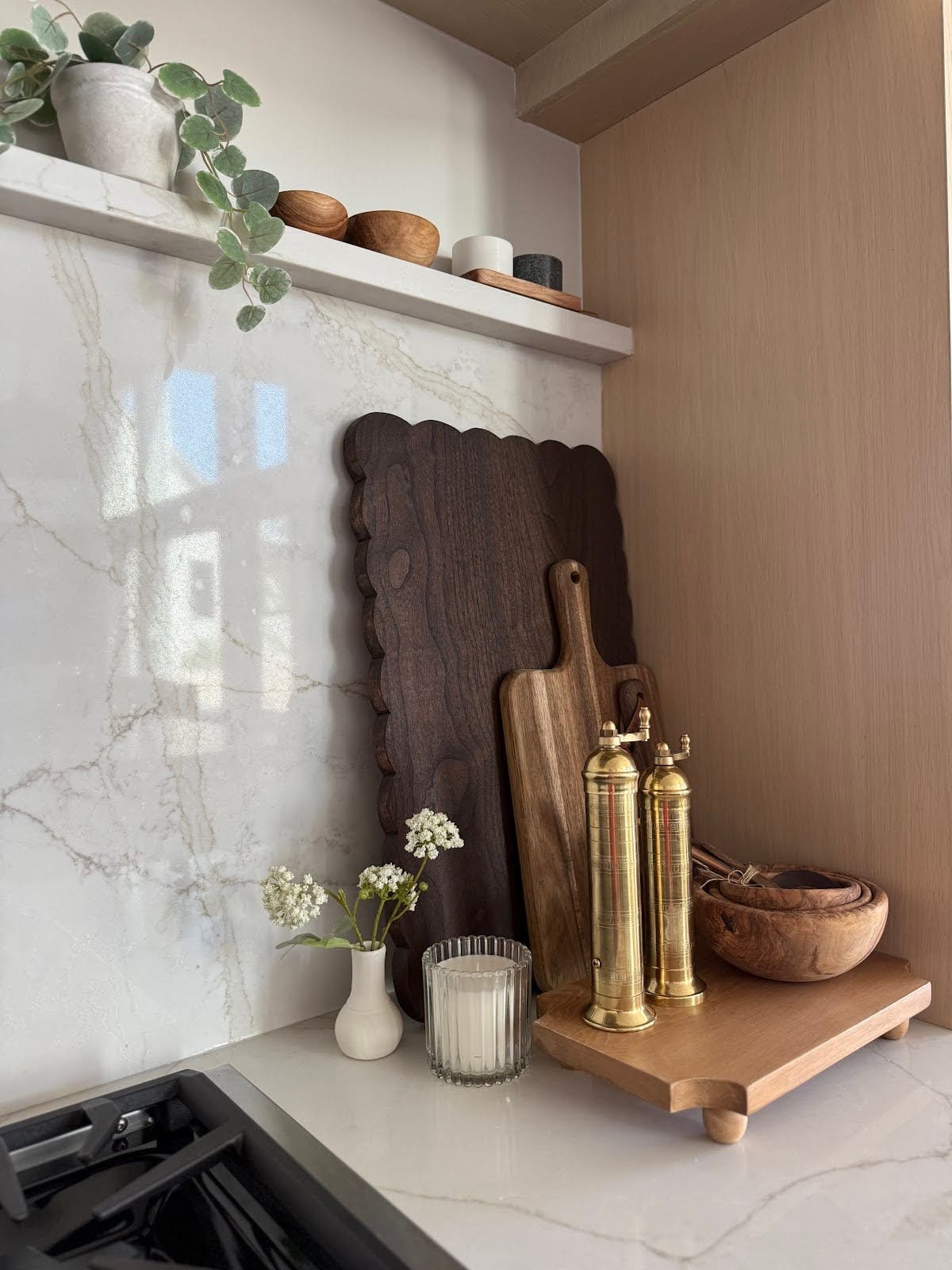 Kitchen countertop with dark scalloped cutting board, gold salt and pepper mills, and wood bowls.