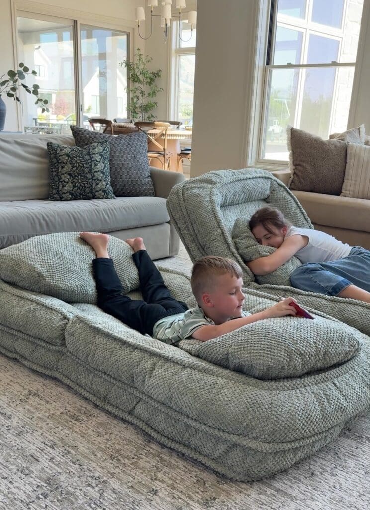 Girl sleeping peacefully on the dog bed while her sister lounges beside her with a puppy and a blanket.