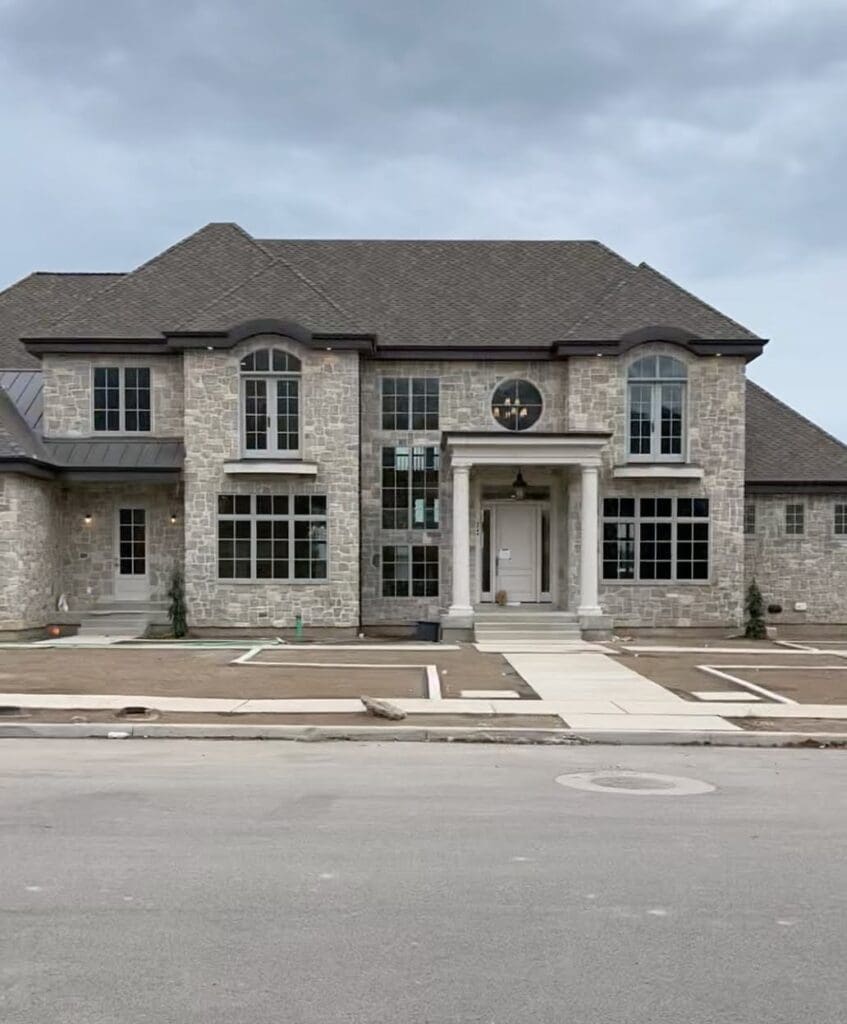Full view of our stone home exterior with gray stone veneer and classic columns, showing symmetrical windows and custom exterior details.