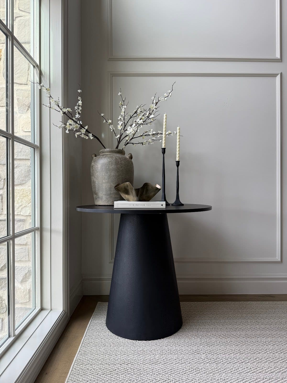 Elegant black pedestal accent table styled with sculptural vase and taper candles in entryway.