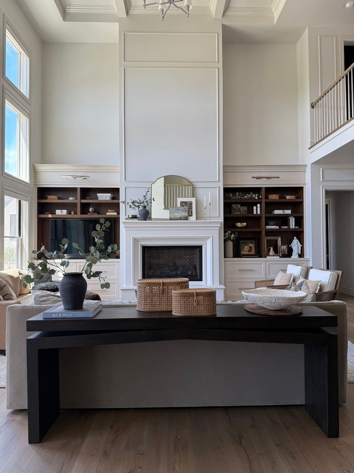 Living room view with black console table behind neutral sofa and tall fireplace surround.