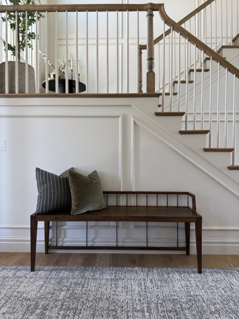 Minimalist entryway with warm wood bench, throw pillows, and board and batten wall molding.