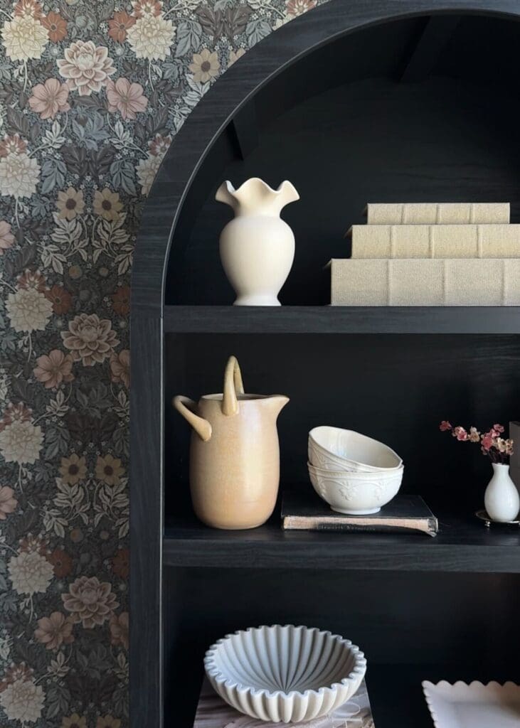 Black arch cabinet styled with ceramic vases, books, brass accents, and decor in formal dining room
