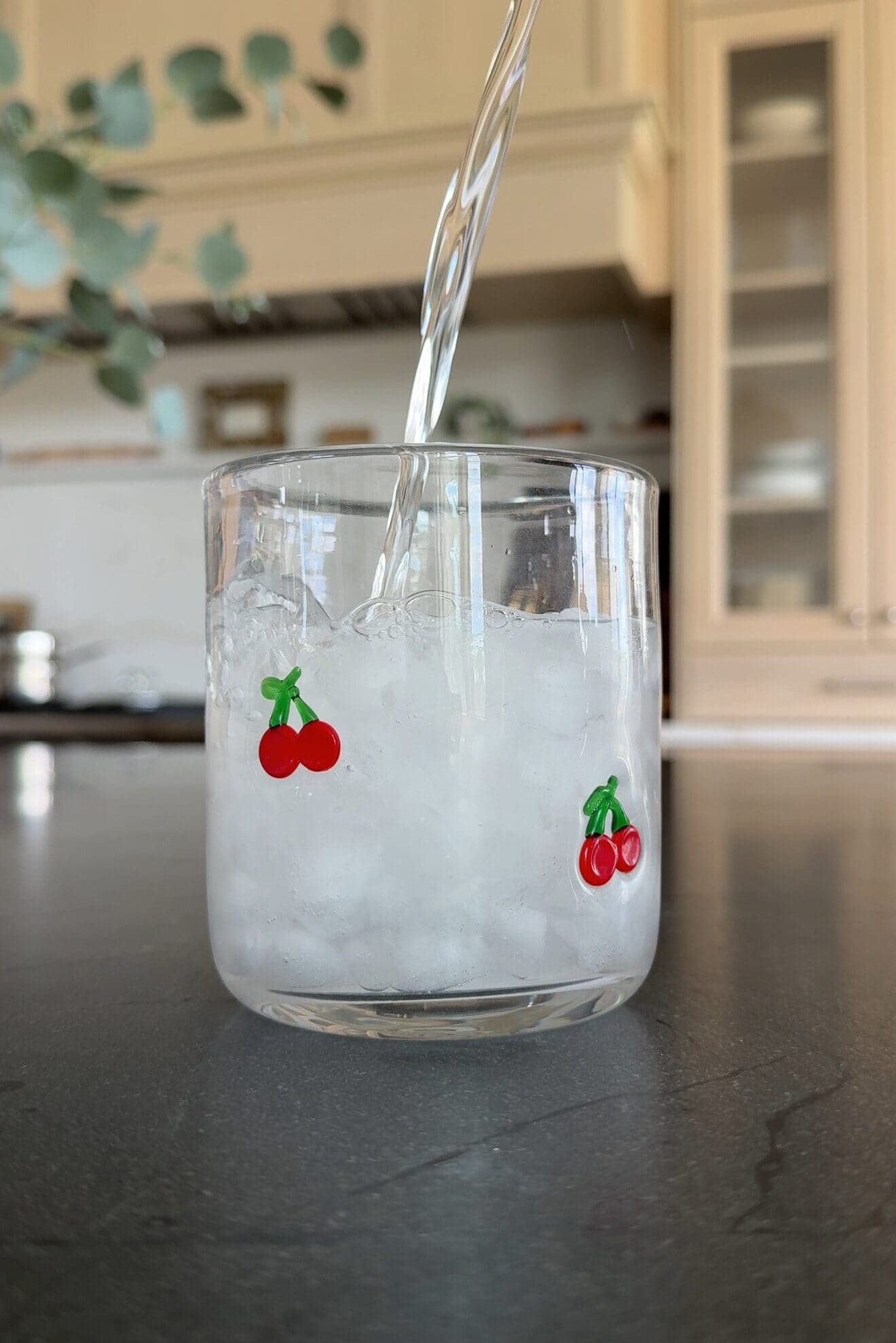 Cherry glass cup being filled with sparkling water over crushed ice
