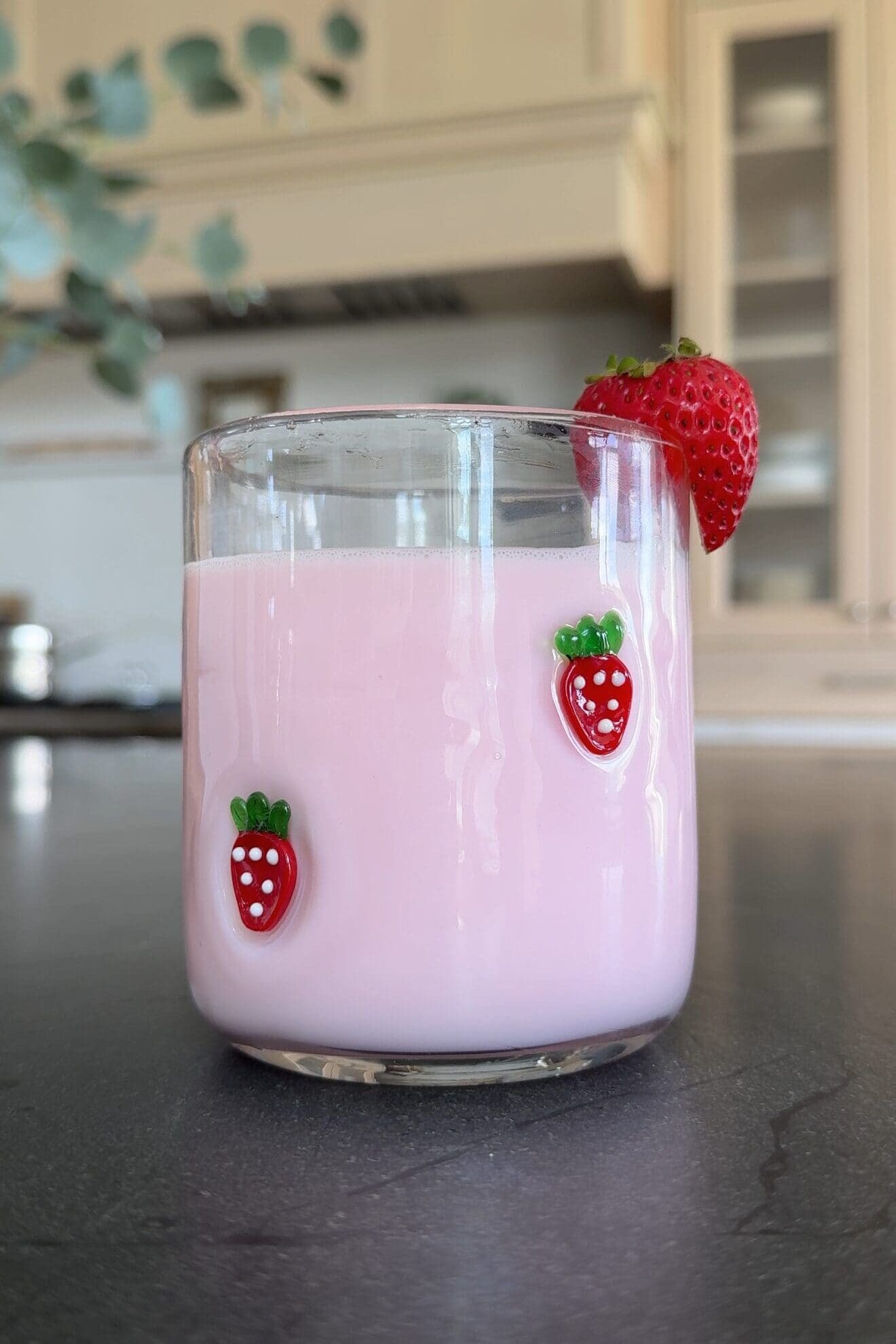 Strawberry glass cup filled with pink milk and garnished with a strawberry on the rim