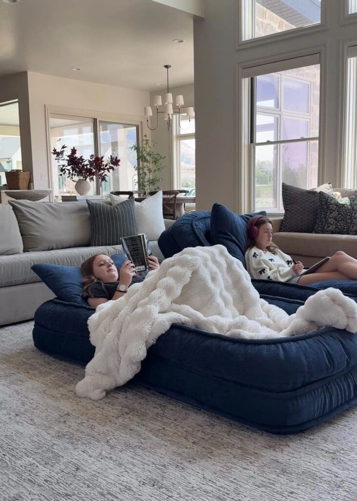 Two girls reading and drawing on the cozy navy floor beds, covered in a faux fur blanket
