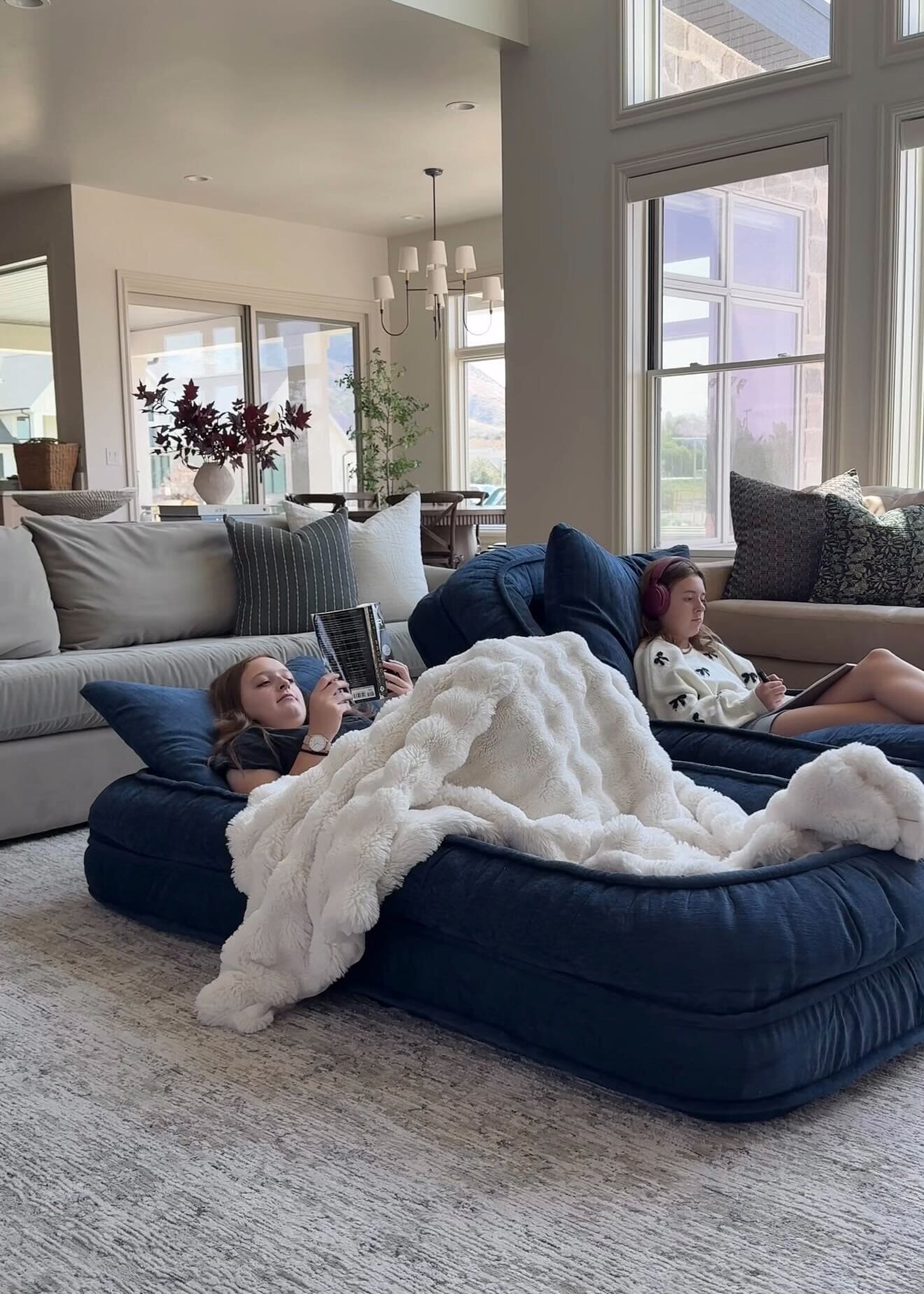 Two girls reading and drawing on the cozy navy floor beds, covered in a faux fur blanket