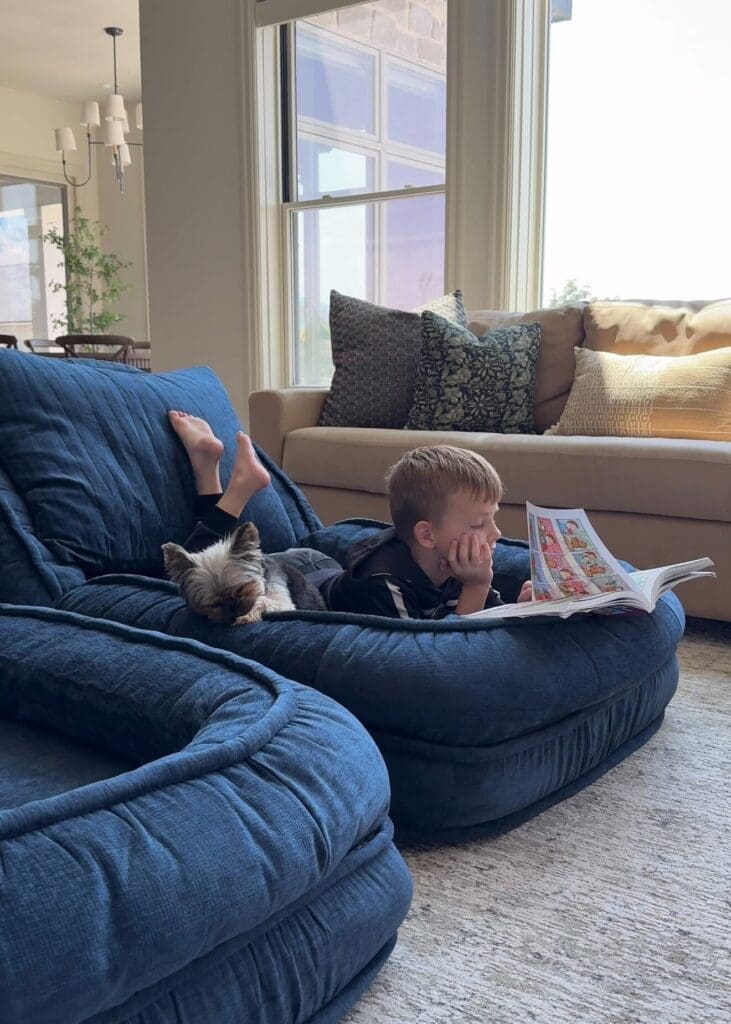 Child and dog lounging side-by-side on the cozy floor bed while reading