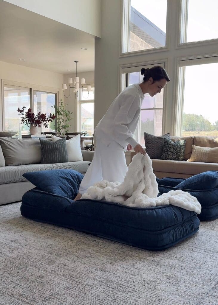 Woman placing a soft blanket on the cozy navy floor bed in a sunlit living room