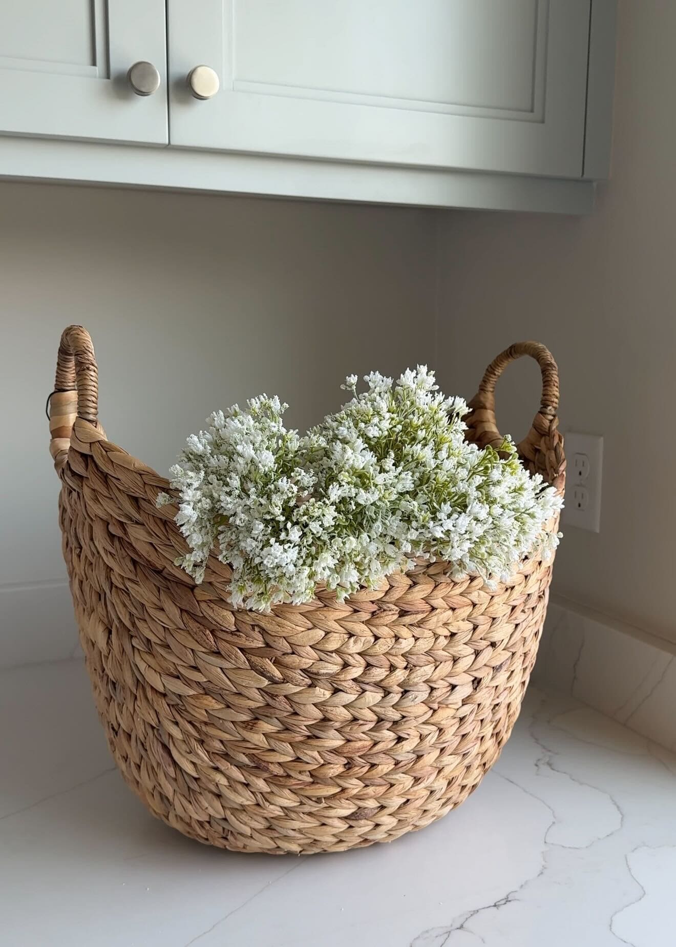 Woven basket with white faux florals on white marble countertop