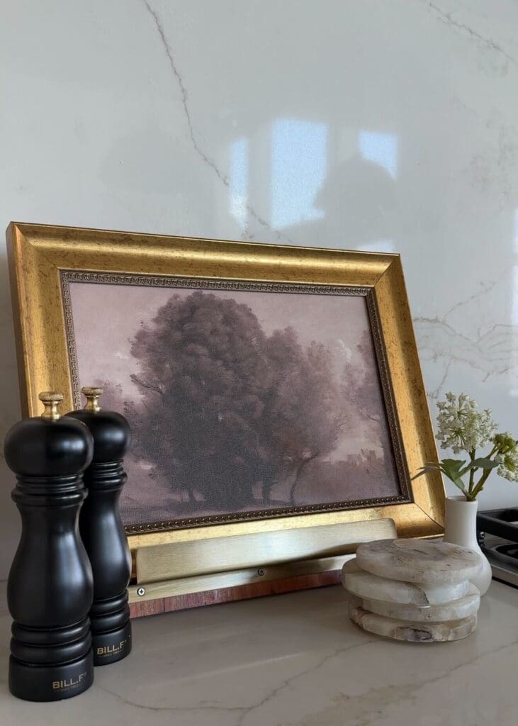 Gold-framed landscape art with black pepper mills and stacked marble coasters