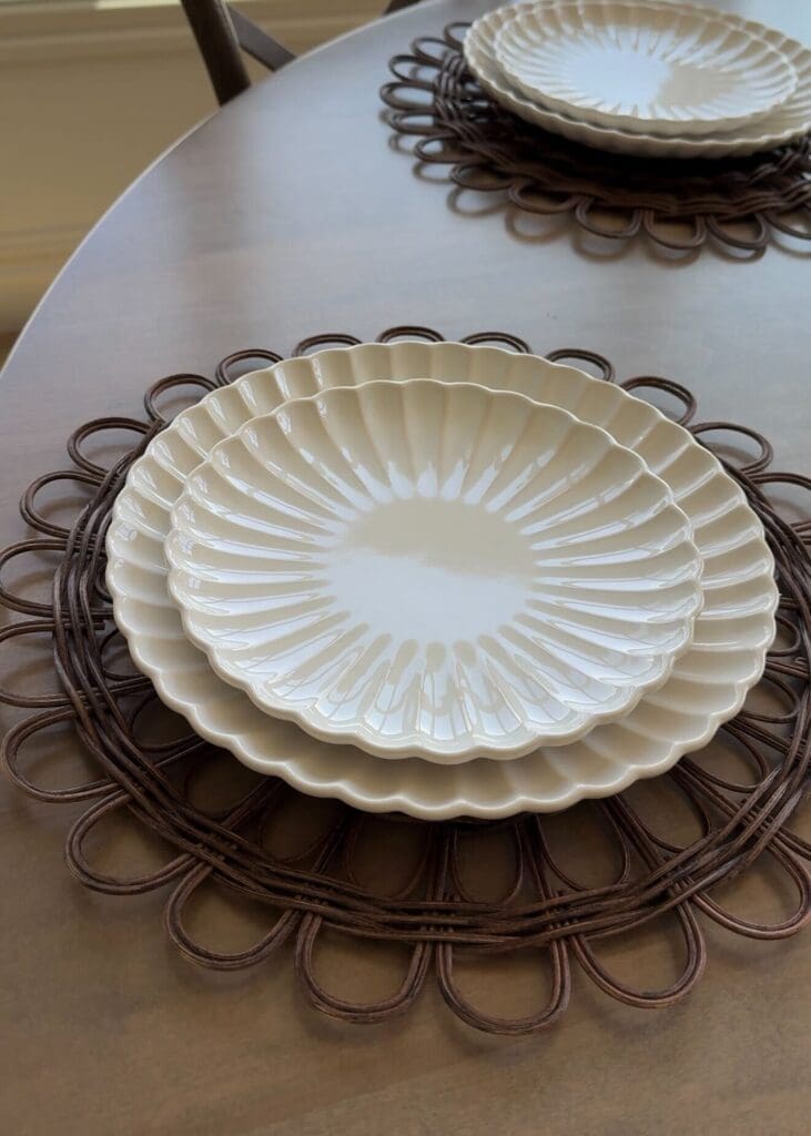 Cream-colored scalloped plates stacked on a brown rattan placemat