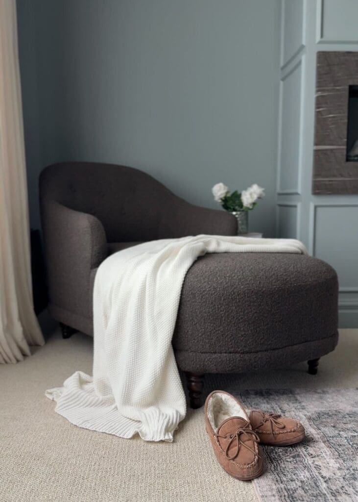 Dark brown bouclé lounge chair with white knit blanket and moccasin slippers