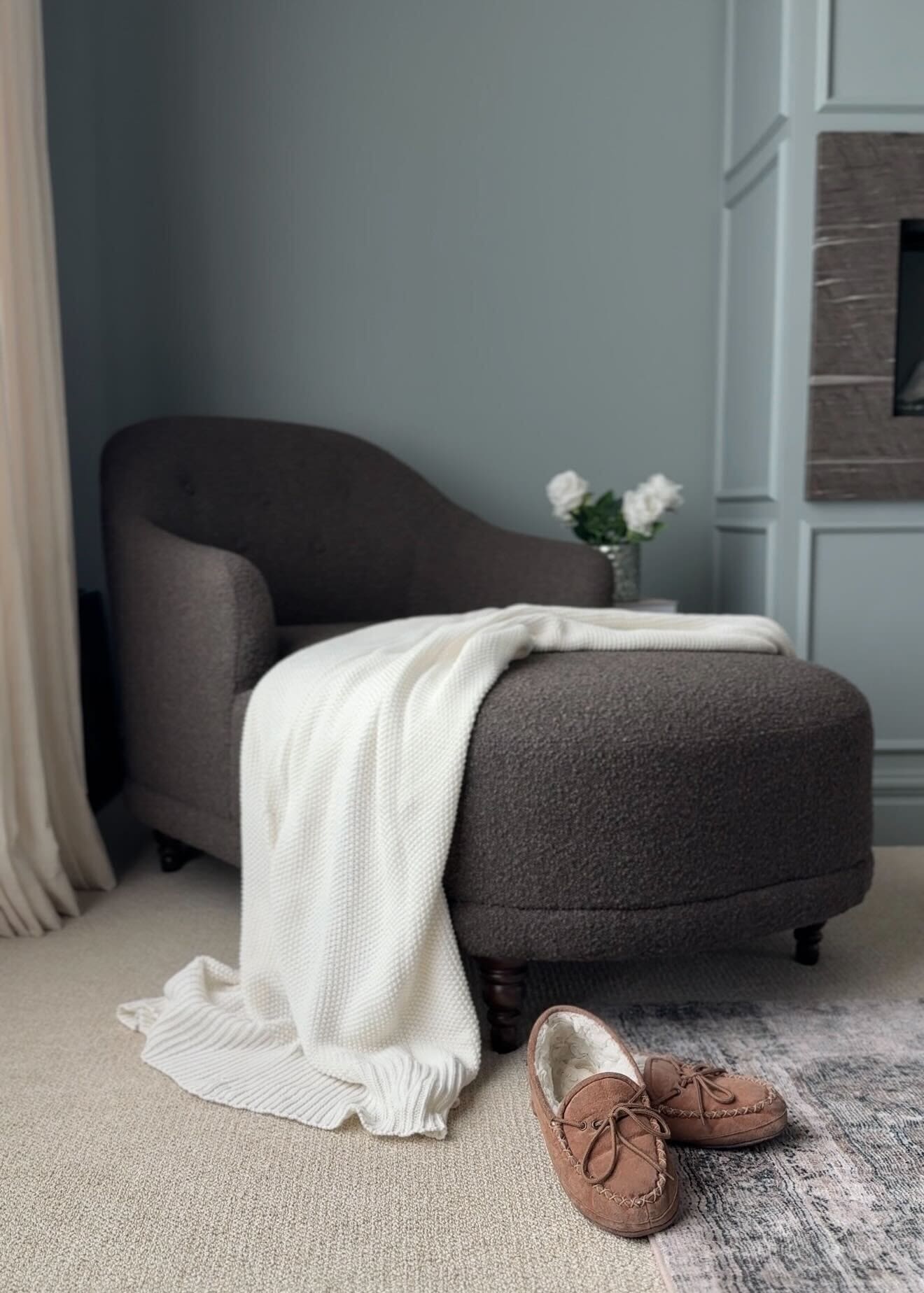 Dark brown bouclé lounge chair with white knit blanket and moccasin slippers