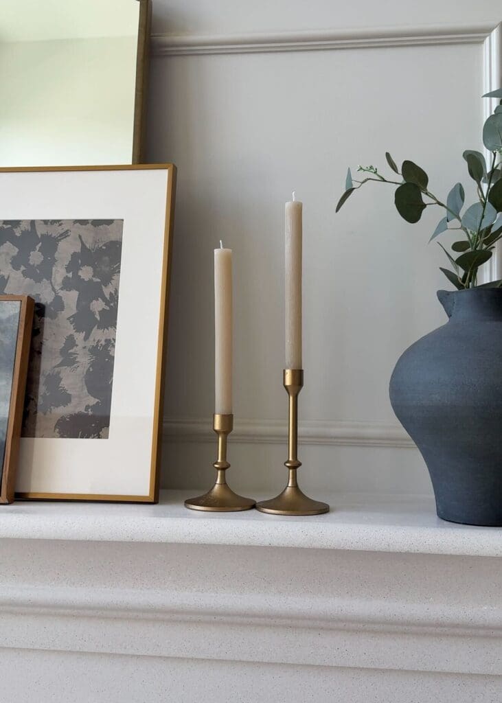 Brass candle holders and layered artwork on a white fireplace mantel