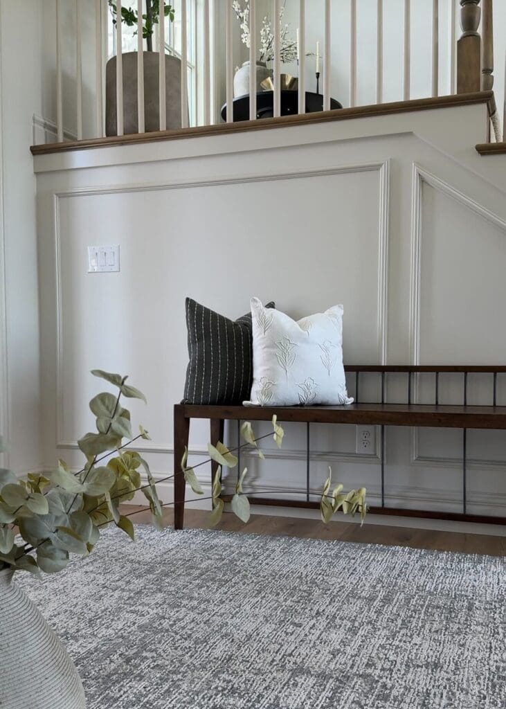 Dark wood bench with striped and floral pillows in front of decorative wall trim