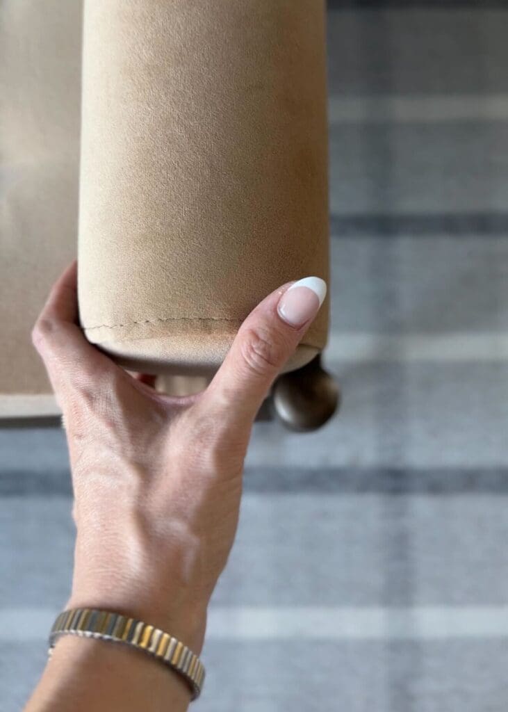 Close-up of fawn velvet bolster end with hand gently touching it, showing soft texture and stitching.