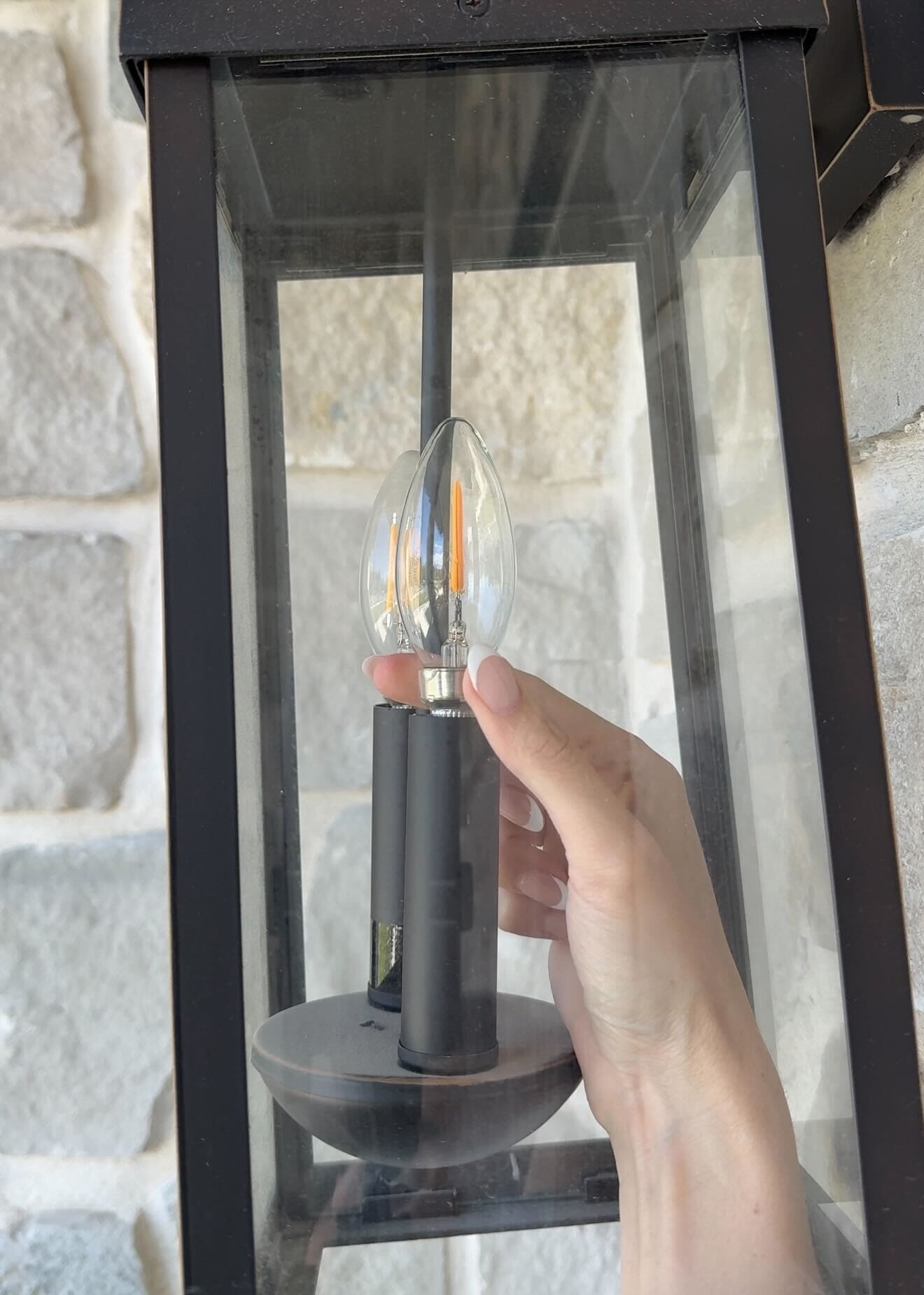 Hand screwing in a flickering LED bulb into black outdoor lantern