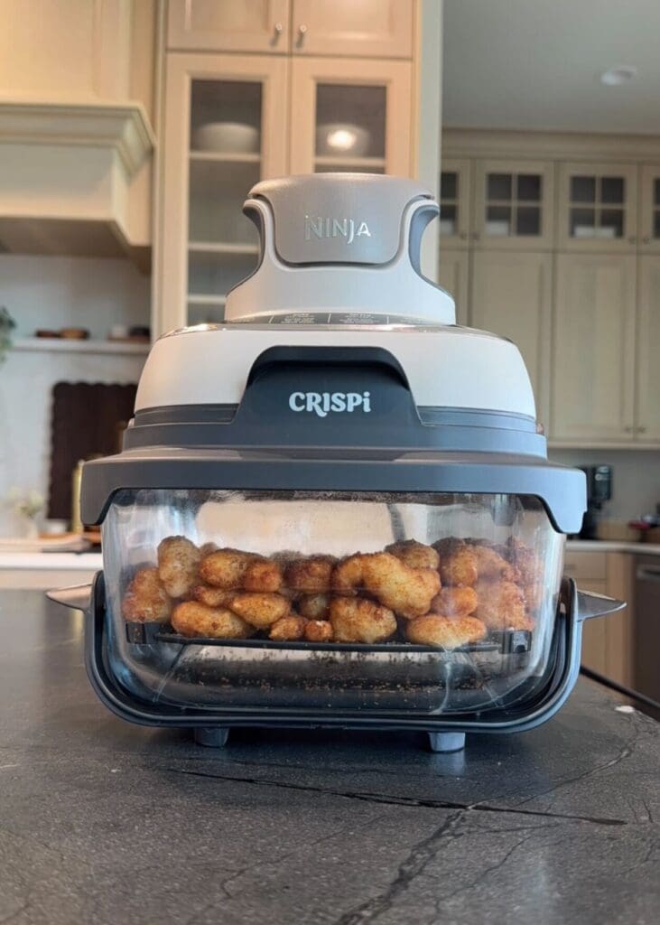 Ninja CRISPi air fryer filled with popcorn shrimp in a kitchen setting