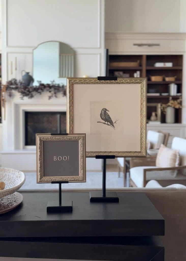 Two gold-framed artworks displayed on adjustable black easels in front of a fireplace.