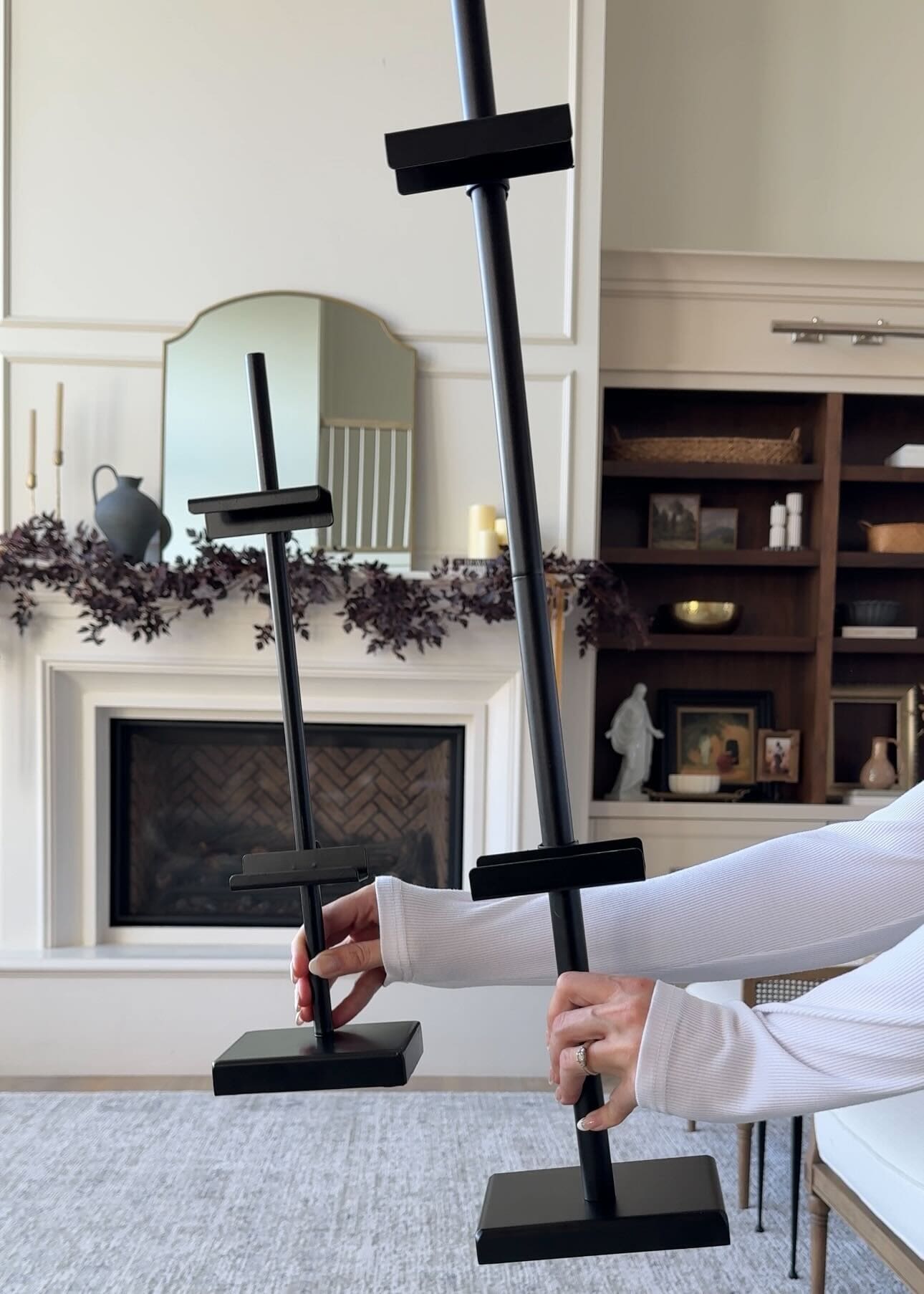 Adjustable black art easels being held up side by side in front of a fireplace