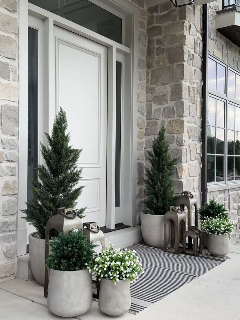 Real home image: neutral stone front porch with potted evergreens and lanterns.