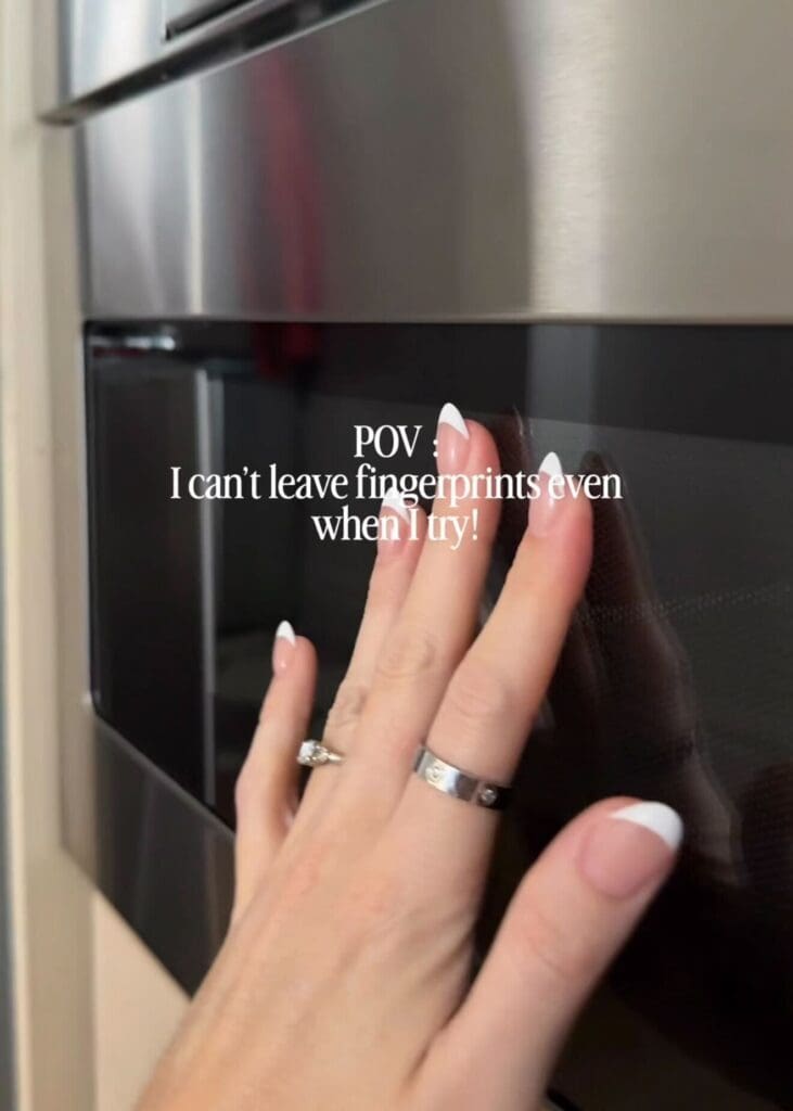 Hand touching a stainless steel microwave showing no fingerprints